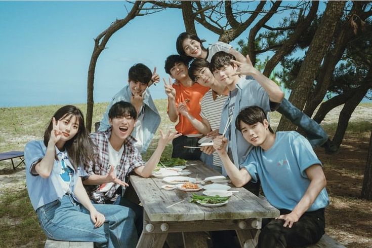 a group of young people sitting around a picnic table eating food and posing for the camera