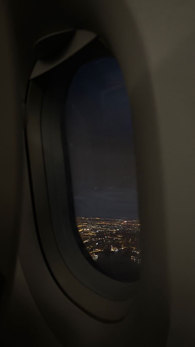 an airplane window with the view of city lights from it's seat area at night