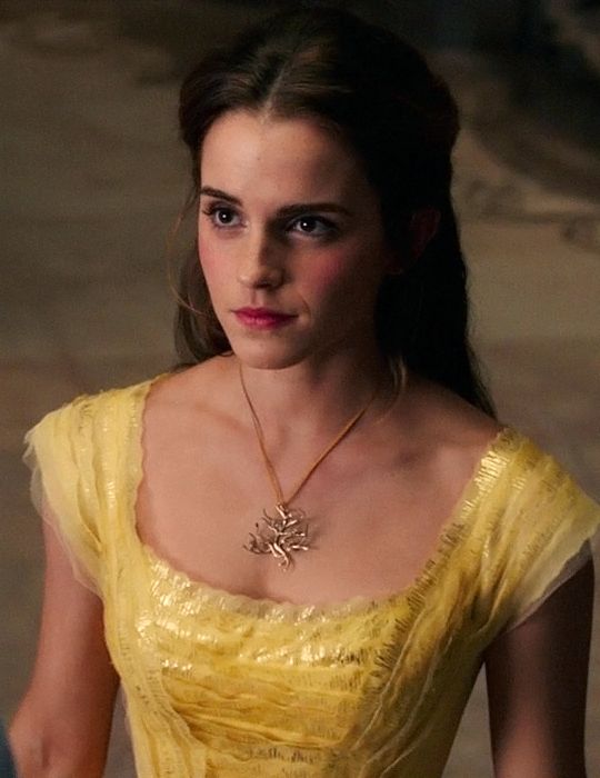 a woman in a yellow dress with a necklace on her neck and hands behind her back