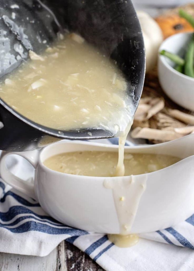 a person pouring gravy into a white bowl on top of a blue and white towel