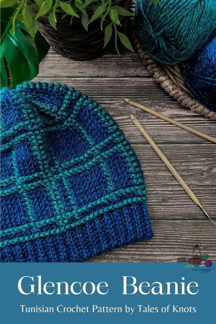 a blue knitted hat sitting on top of a wooden table next to knitting needles