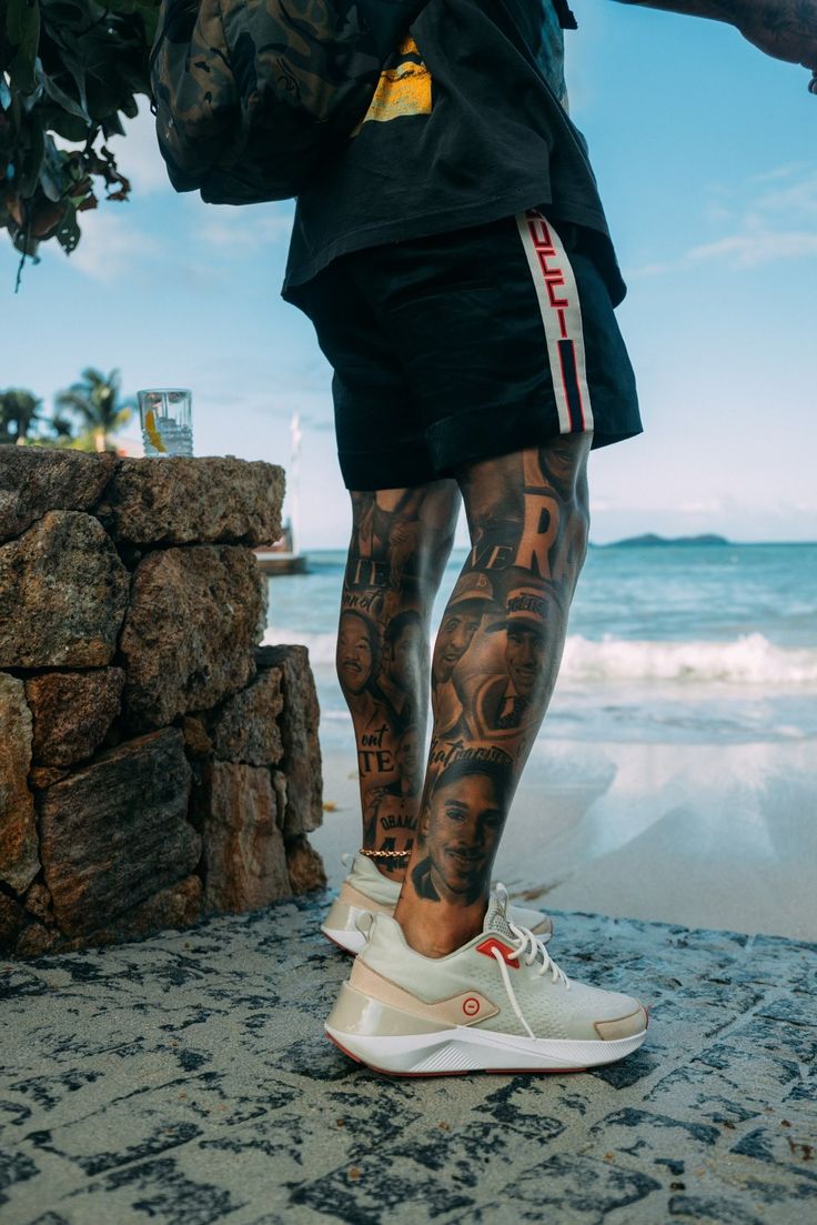 a man with tattoos on his legs standing next to the ocean