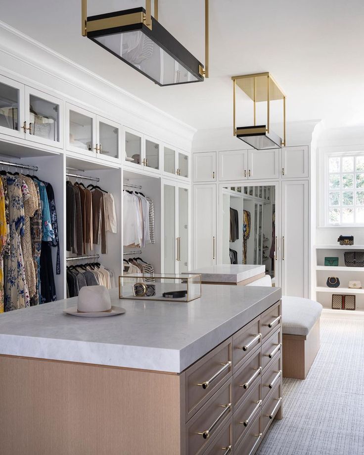 a walk - in closet with white cabinets and gold handles, drawers, and clothes on hangers