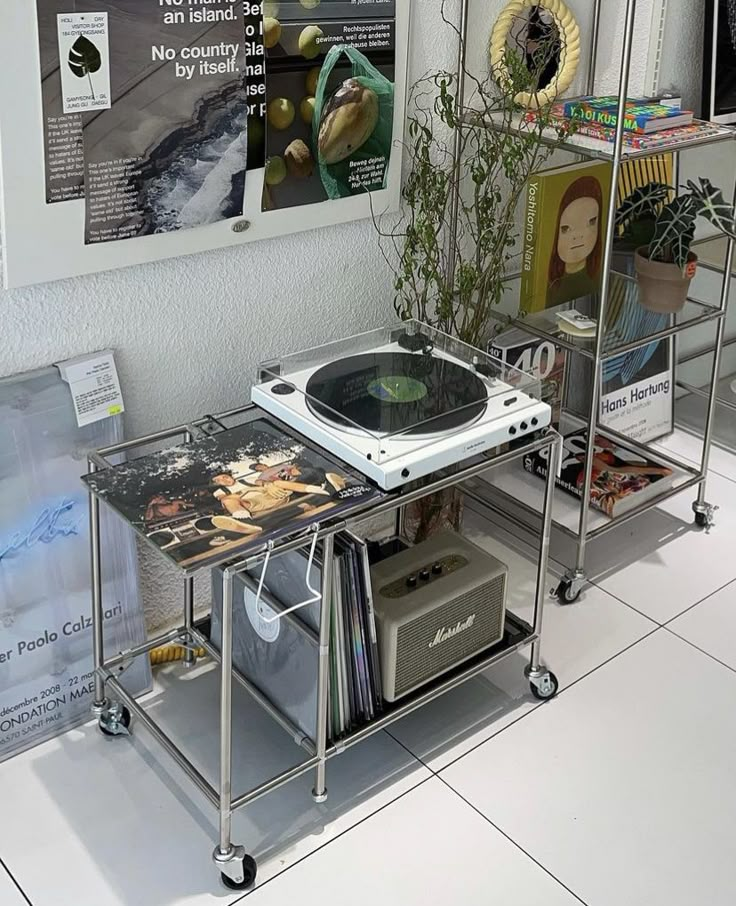 a record player sitting on top of a metal cart next to a wall with posters