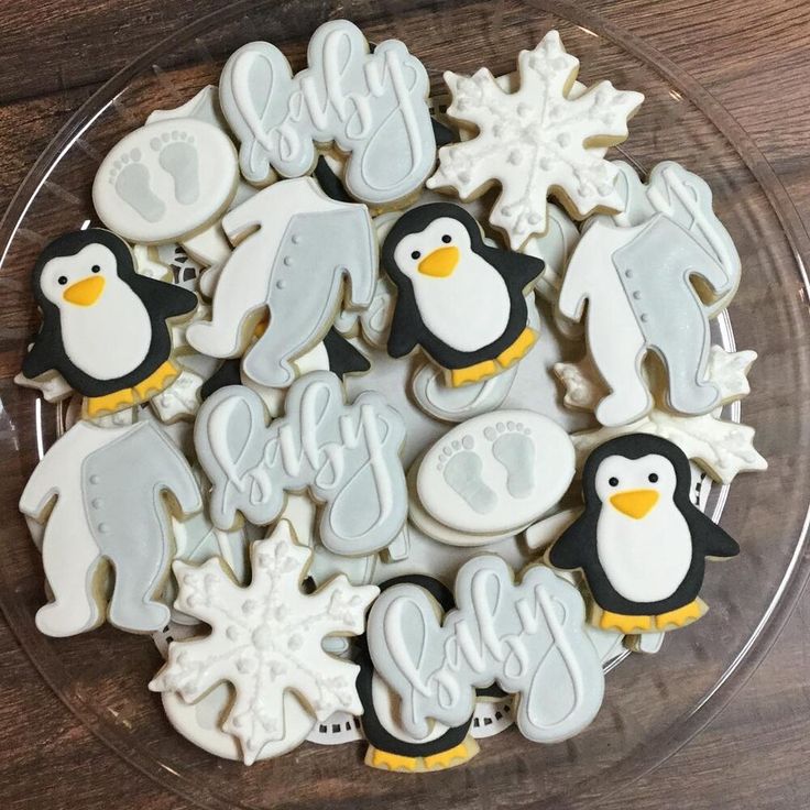 decorated cookies in the shape of penguins and snowflakes on a glass platter