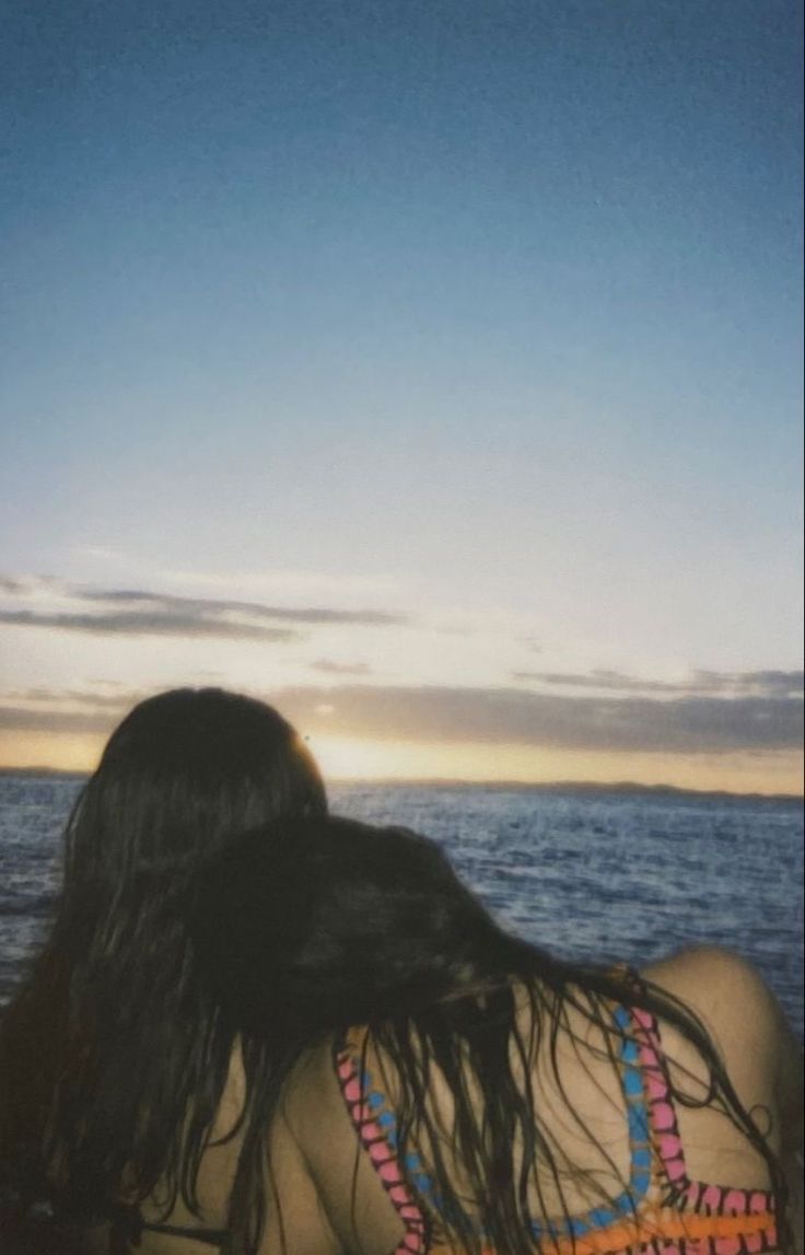 the back of a woman's head as she sits in front of the ocean