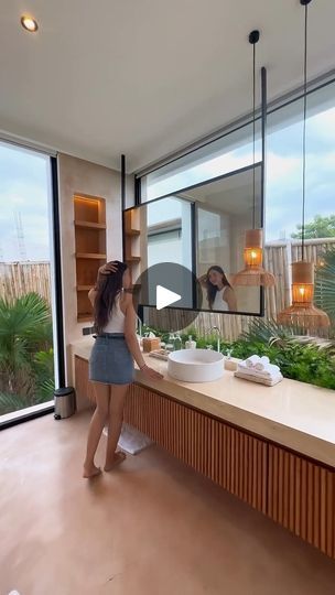 a woman standing in front of a bathroom sink next to a window with plants on it