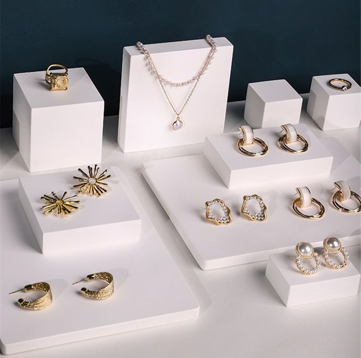 several different types of rings and necklaces displayed on white pedestals with blue wall in background