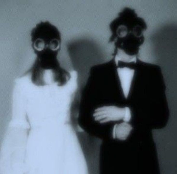 two people wearing gas masks standing next to each other in front of a white wall