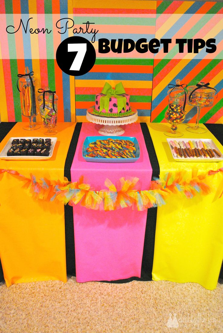 a table topped with lots of desserts and candy on it's sides in front of a colorful wall