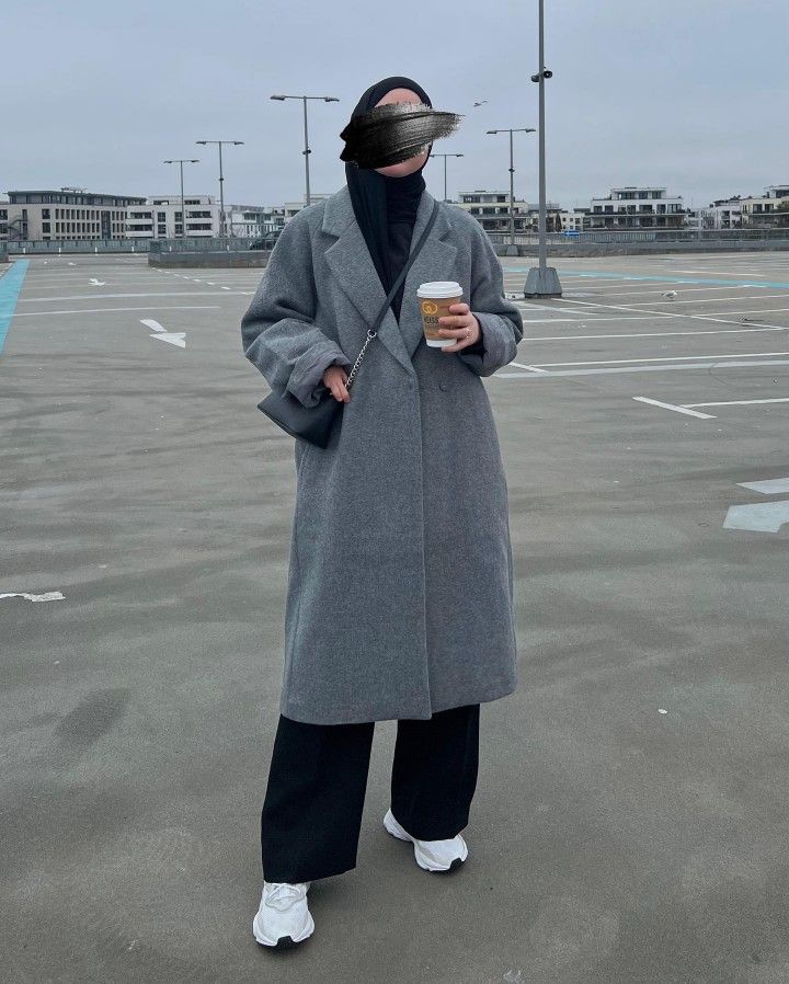 a person standing in an empty parking lot wearing a coat and holding a coffee cup