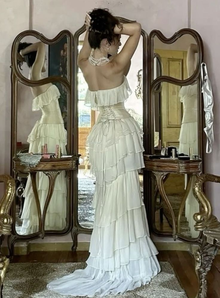 a woman standing in front of a mirror wearing a white dress with ruffles