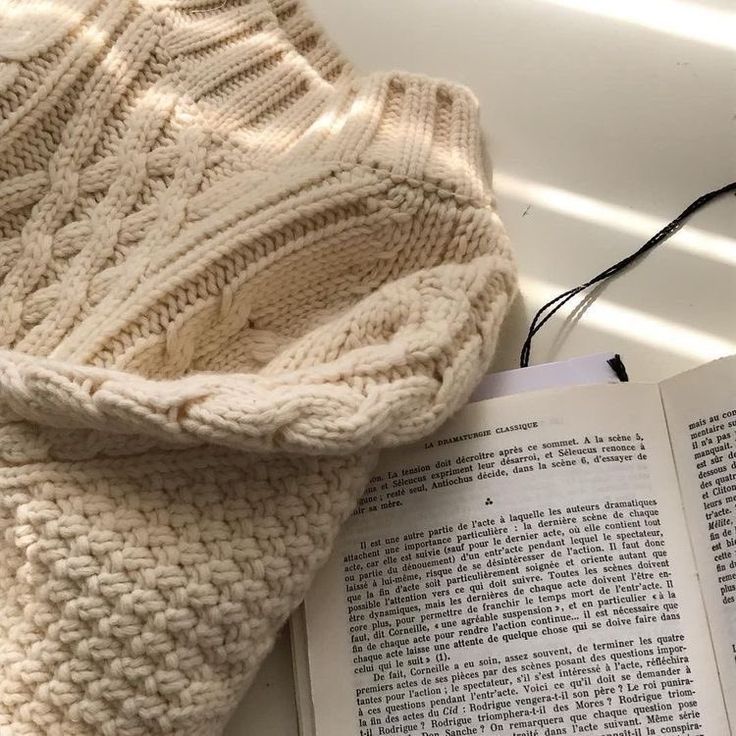 an open book laying next to a knitted sweater