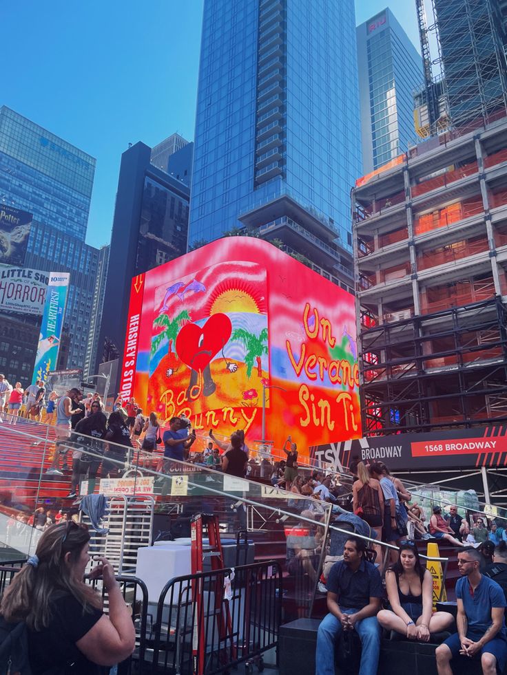 people are sitting on benches in front of a large billboard that reads one very sunny day