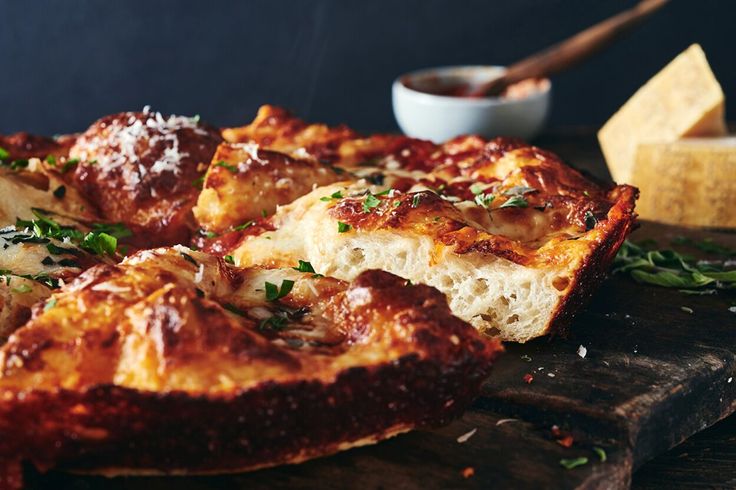 a deep dish pizza with cheese and herbs on a wooden cutting board next to a bowl of dipping sauce