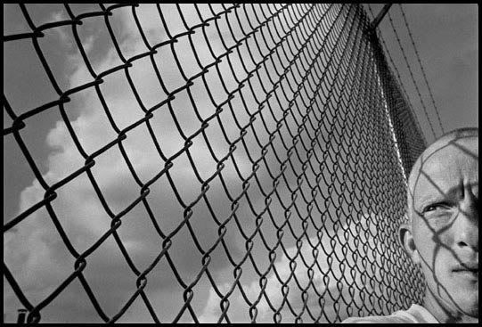 a man standing next to a fence holding a tennis racquet