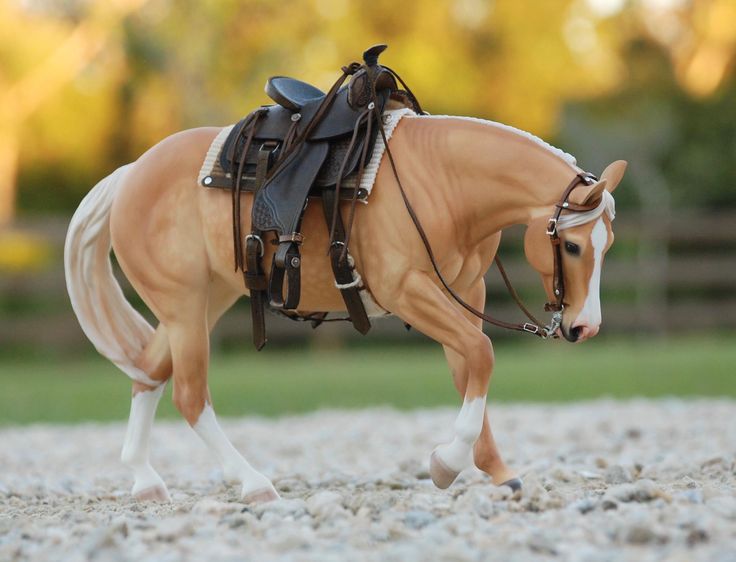 a toy horse that is standing in the gravel with it's bridle on