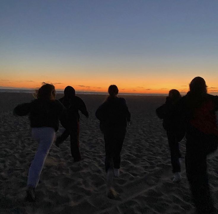 four people walking on the beach at sunset