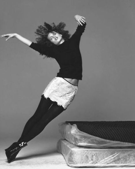 a woman in black and white is posing with her arms spread out as she stands next to a mattress