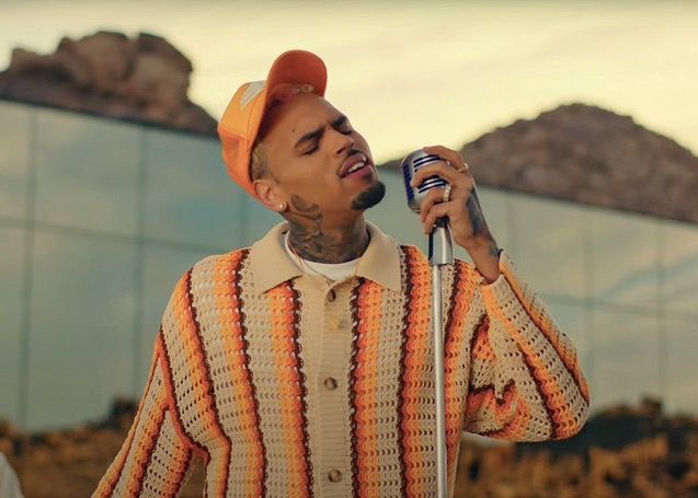 a man in an orange and white shirt holding a microphone with his right hand up to his ear