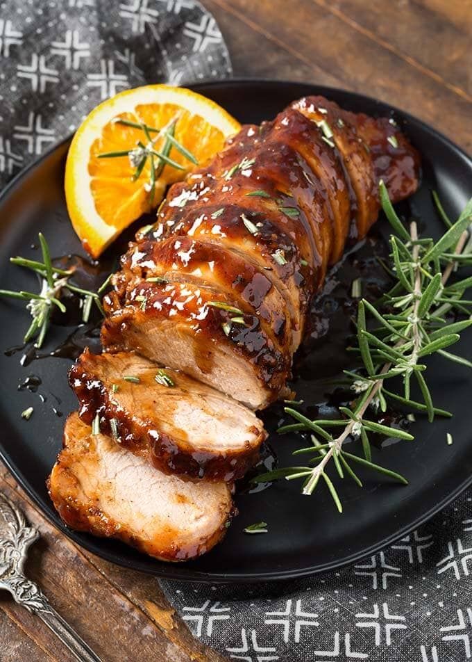 a black plate topped with meat covered in sauce and garnished with fresh herbs