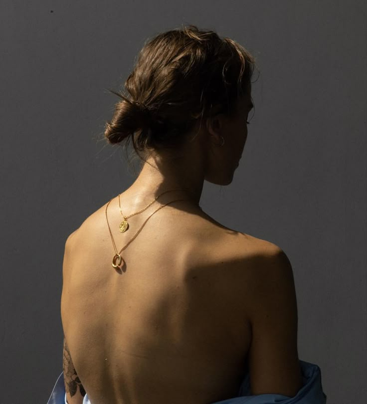 the back of a woman wearing a blue dress with a gold necklace on her neck