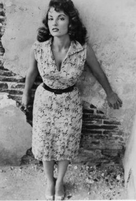 an old black and white photo of a woman leaning against a wall with her hands on her hips