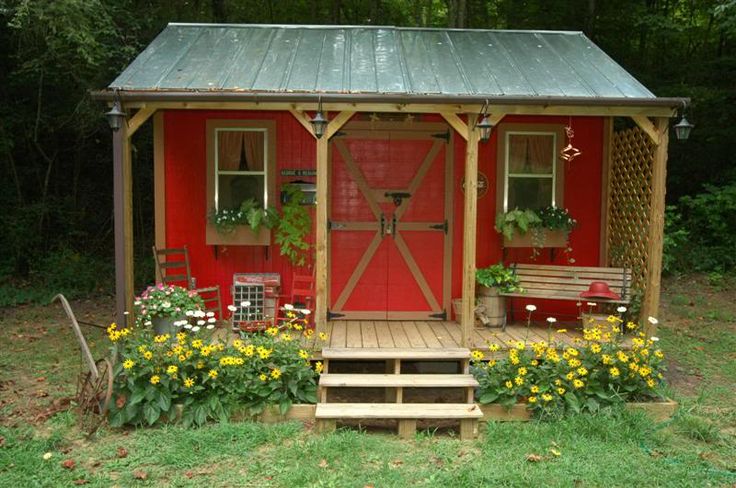 a small red shed sitting in the middle of a field with flowers and plants around it