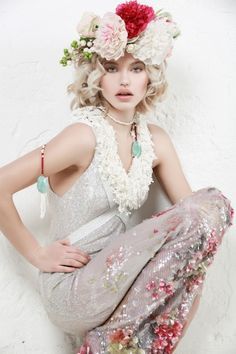 a woman with flowers in her hair sitting on the ground wearing a dress and necklace