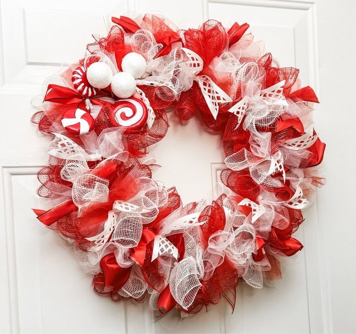 a red and white christmas wreath hanging on a door