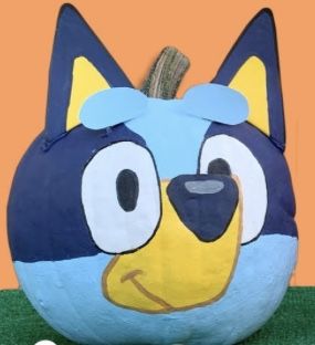 a blue and yellow stuffed animal sitting on top of a green field next to a pumpkin