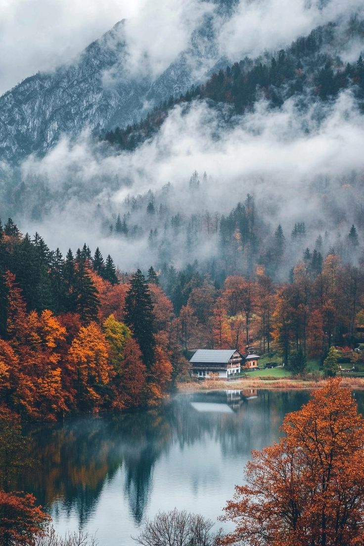 a lake surrounded by trees and fog in the sky with mountains in the back ground