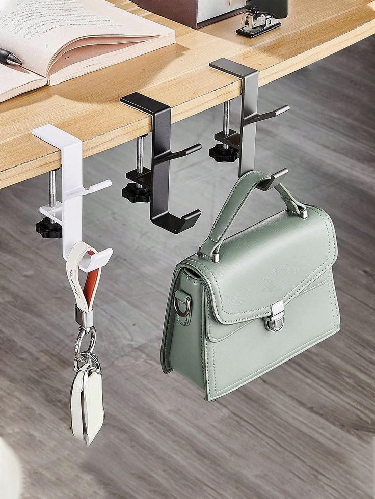 two purses hanging from hooks on a table with a book and other items in the background