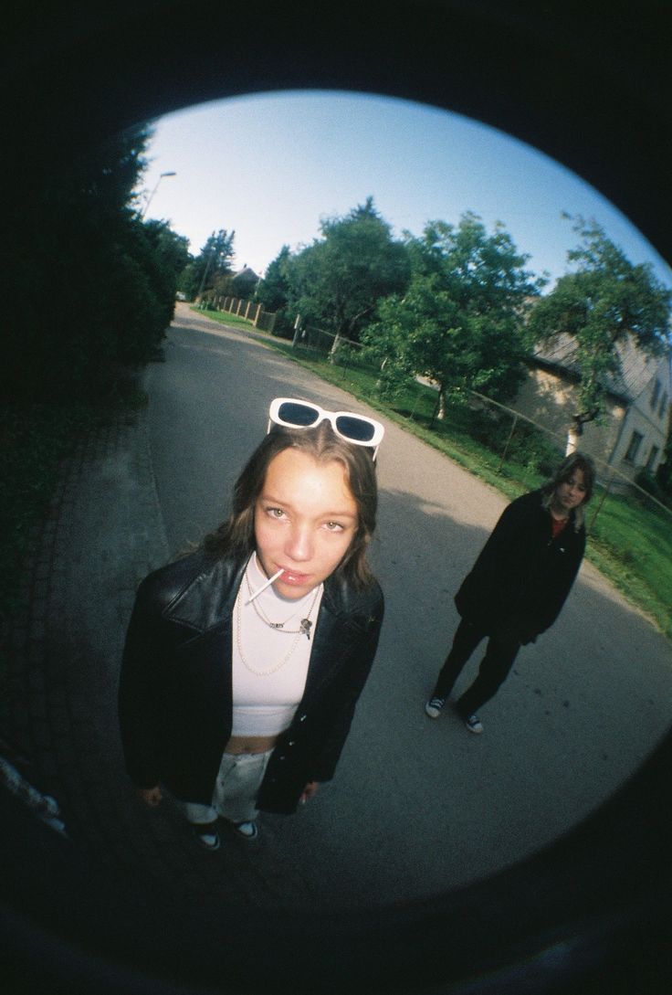 two people standing on the side of a road with sunglasses on their heads and one person wearing