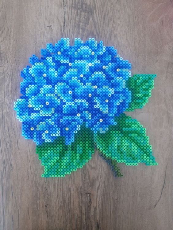 a blue flower with green leaves on a wooden surface, made out of perler beads