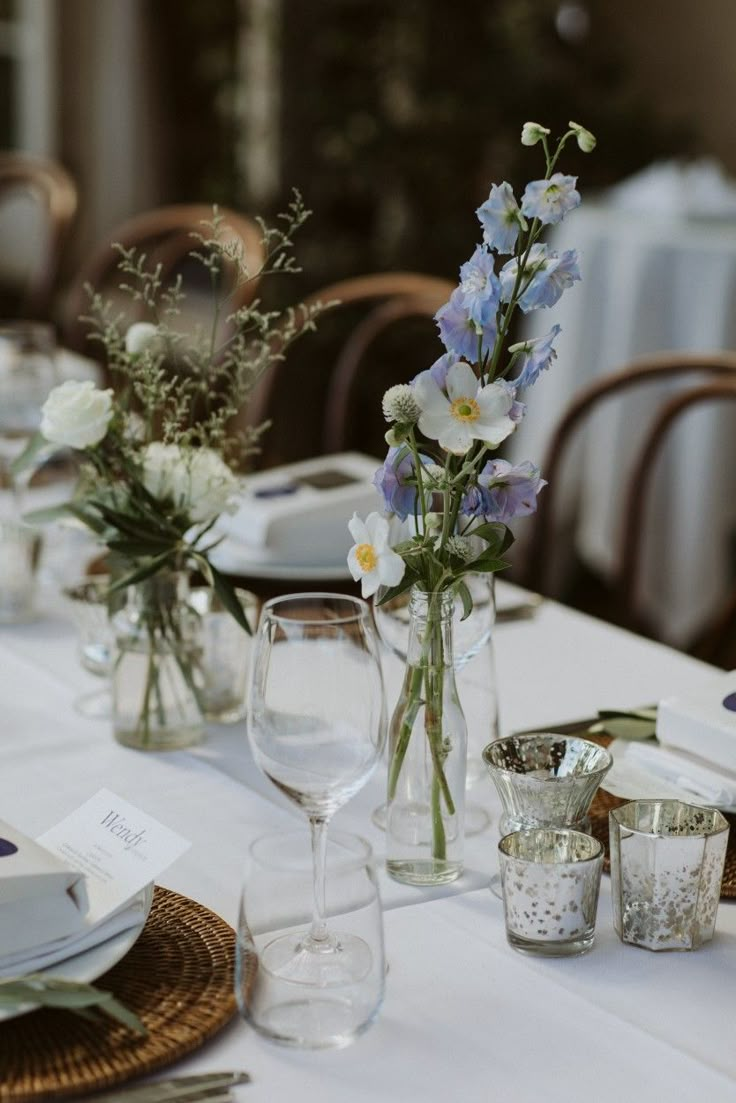 the table is set with glasses, plates and flowers