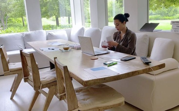 a woman sitting at a table with a laptop on her lap talking on the phone