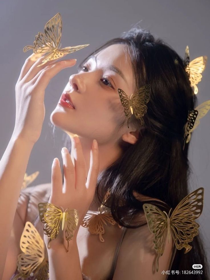 a woman with gold butterflies on her head and hands in front of her face, looking up at the sky