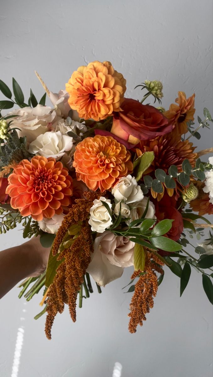 a bouquet of flowers is being held by someone's hand in front of a white wall