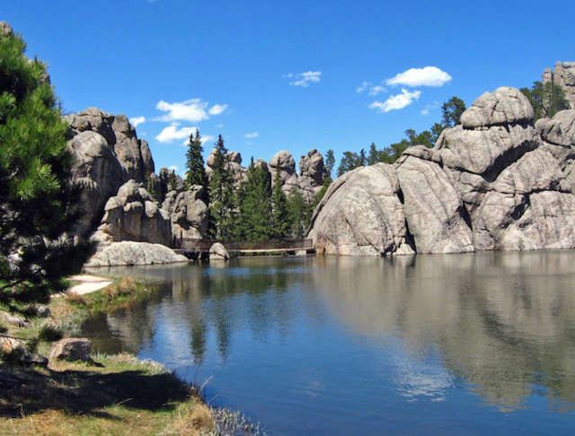 a lake surrounded by rocks and trees under a blue sky