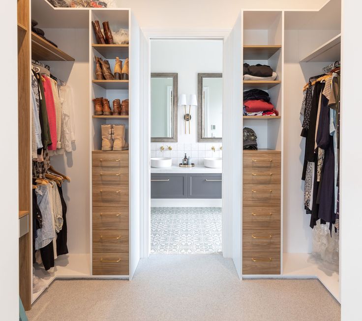 a walk in closet with two sinks and open shelving units on both sides, full of clothes