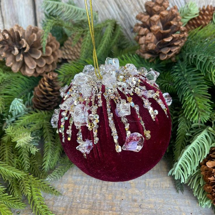 a red ornament hanging from a christmas tree with pine cones and evergreen needles