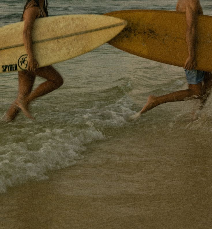 two people walking into the water with surfboards in their hands and one person holding a surfboard