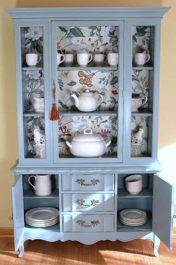 the china cabinet is painted blue and has many dishes on it