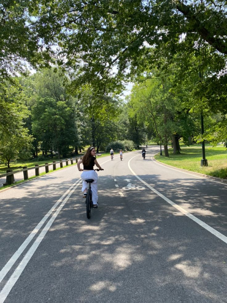 a person riding a bike down a tree lined street with people on bikes in the distance