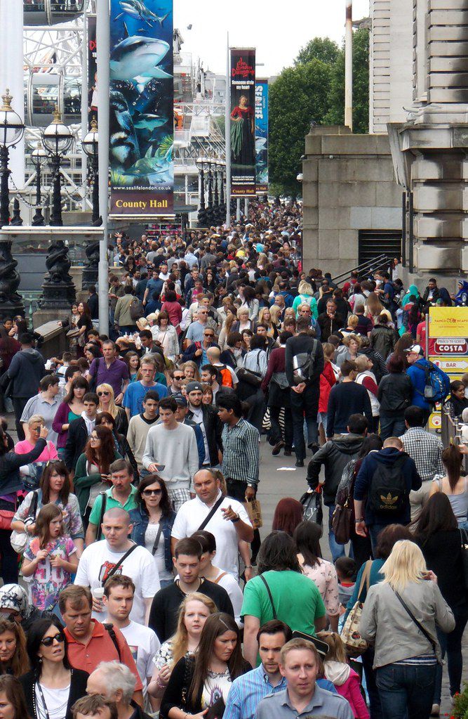 a large crowd of people walking down a street next to tall buildings and signs on the side walk