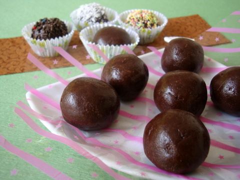 chocolate balls on a plate with pink and white paper wrappers next to them,