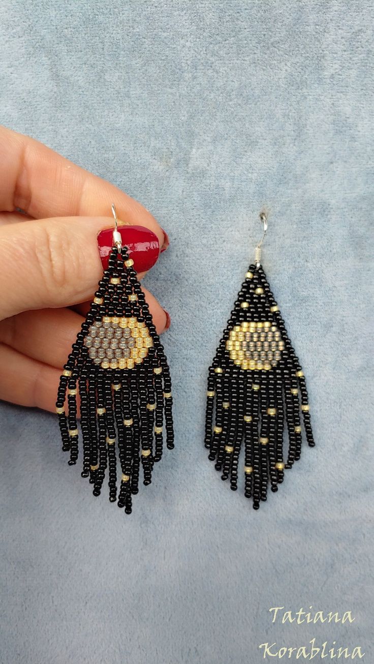 a pair of black and gold beaded earrings on a woman's hand with red nail polish