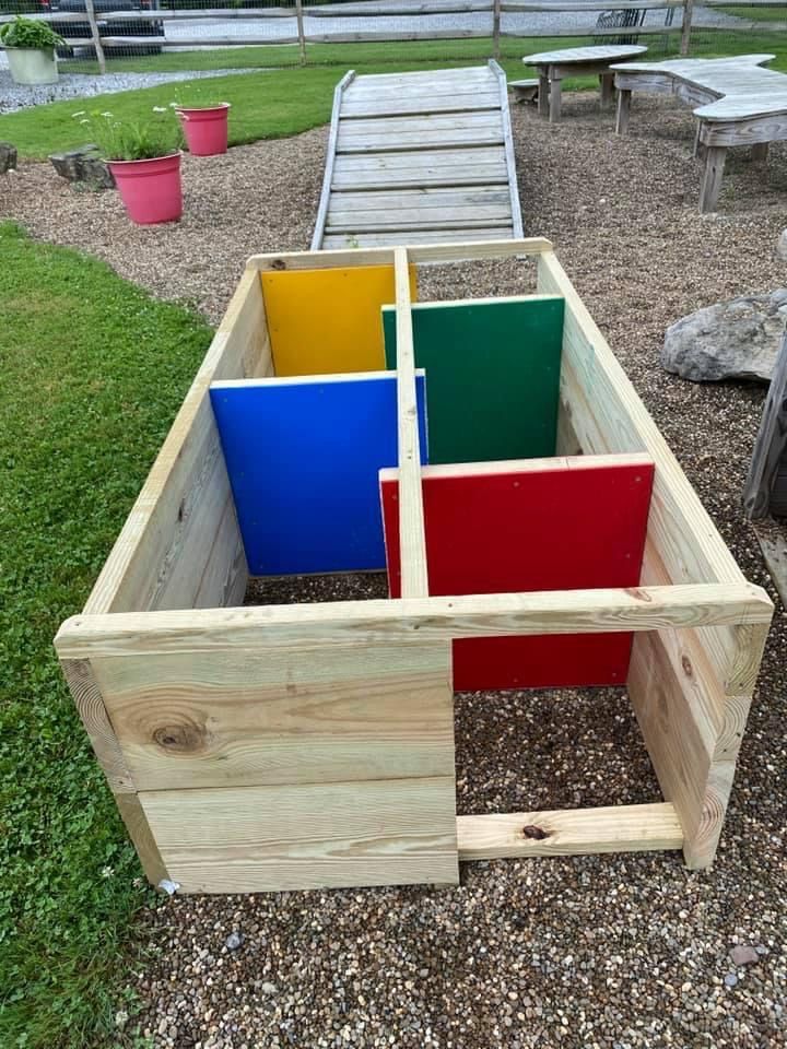 an outdoor play area made out of wood and colored plastic bins on the ground