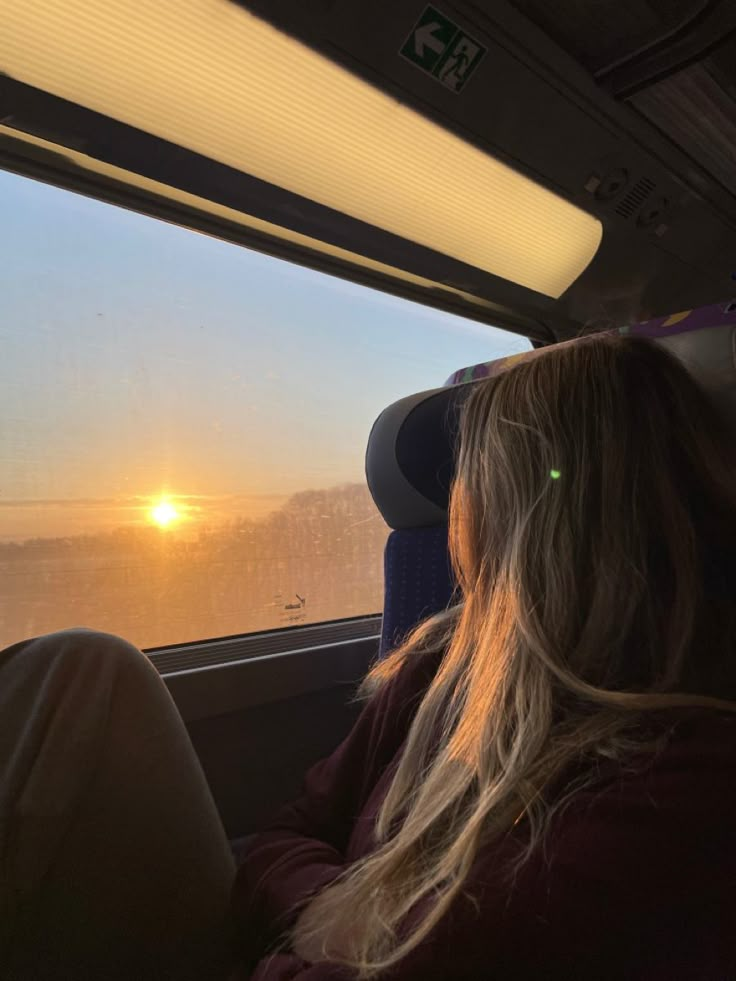 a woman sitting on a bus looking out the window at the sun setting in the distance